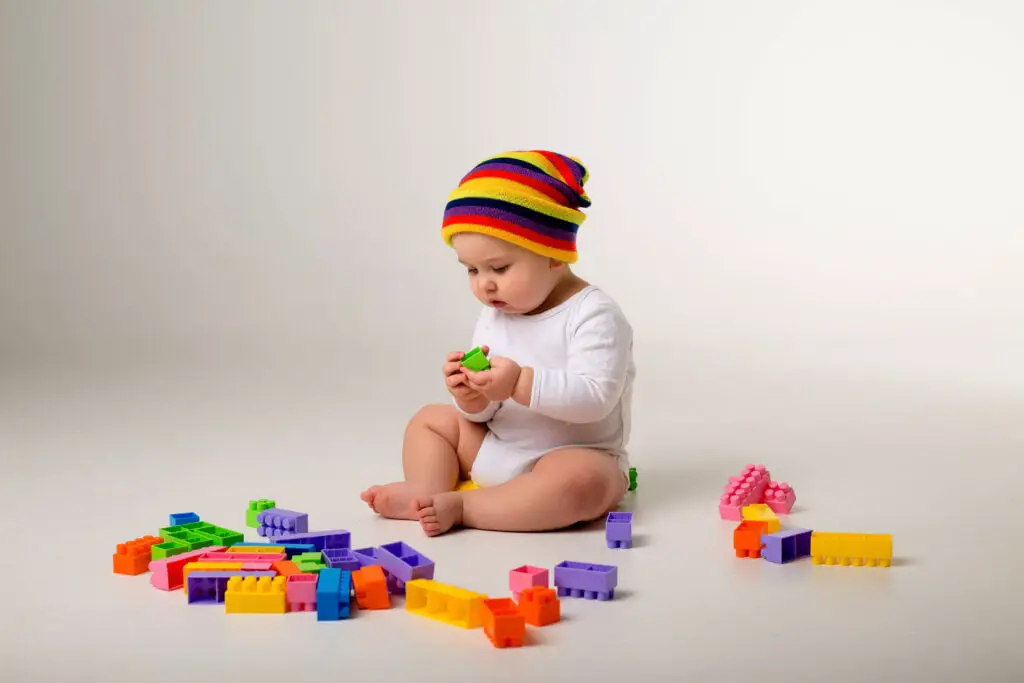 baby boy playing with multi colored constructor on white wall 1024x683 1